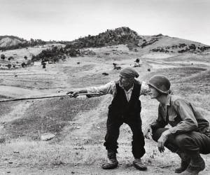 Immagine di Robert Capa, Un contadino siciliano indica a un ufficiale americano la direzione presa dai tedeschi, nei pressi di Troina, 4-5 agosto 1943